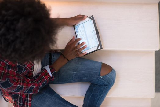 Attractive young black woman using her electronic tablet while sitting on a staircase