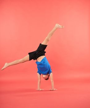 Adorable male child in sportswear standing upside down and doing splits while performing handstand stunt