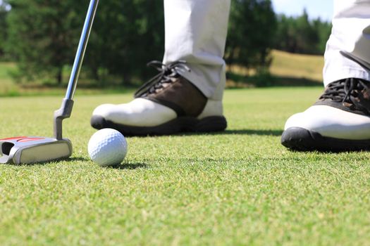 Golf player at the putting green hitting ball into a hole