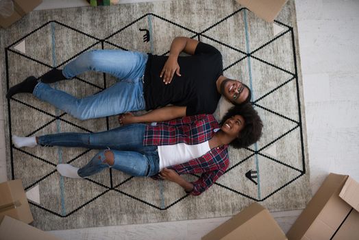 Top view of attractive young African American couple moving, holding hands, looking at camera and smiling while lying among cardboard boxes