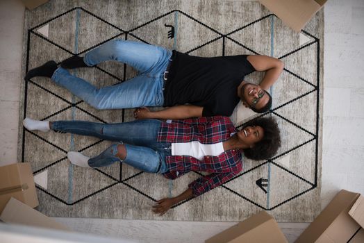 Top view of attractive young African American couple moving, holding hands, looking at camera and smiling while lying among cardboard boxes