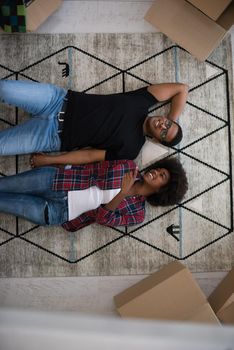 Top view of attractive young African American couple moving, holding hands, looking at camera and smiling while lying among cardboard boxes