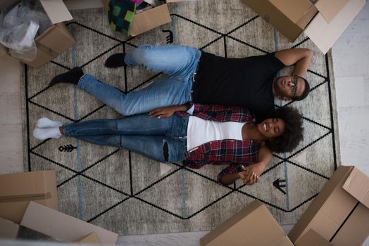 Top view of attractive young African American couple moving, holding hands, looking at camera and smiling while lying among cardboard boxes