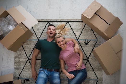 Top view of attractive young couple moving, holding hands, looking at camera and smiling while lying among cardboard boxes