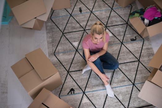 top view of young beautiful woman sitting and relaxing on the floor after moving into a new home with cardboard boxes around her