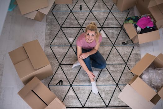 top view of young beautiful woman sitting and relaxing on the floor after moving into a new home with cardboard boxes around her