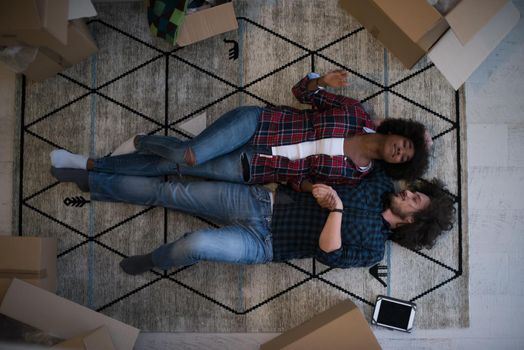 Top view of attractive young multiethnic couple moving, holding hands, looking at camera and smiling while lying among cardboard boxes