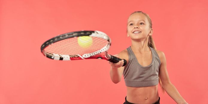 Adorable girl tennis player wearing sports crop top while bouncing tennis ball on racket and smiling