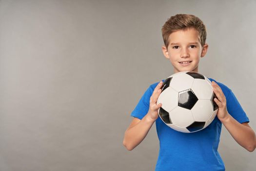 Cute male child football player looking at camera and smiling while holding soccer ball
