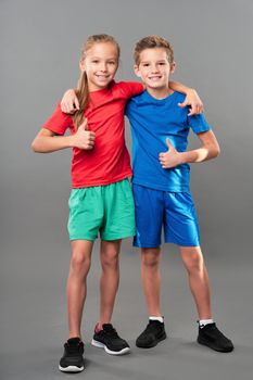 Adorable kids showing approval gesture and smiling while standing against gray background