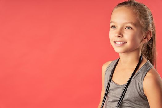 Cute joyful girl with skipping rope around her neck looking away and smiling