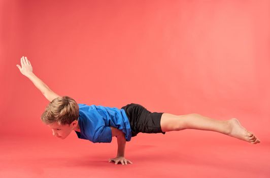 Cute male child in shorts balancing on one hand and looking away. Isolated on red background