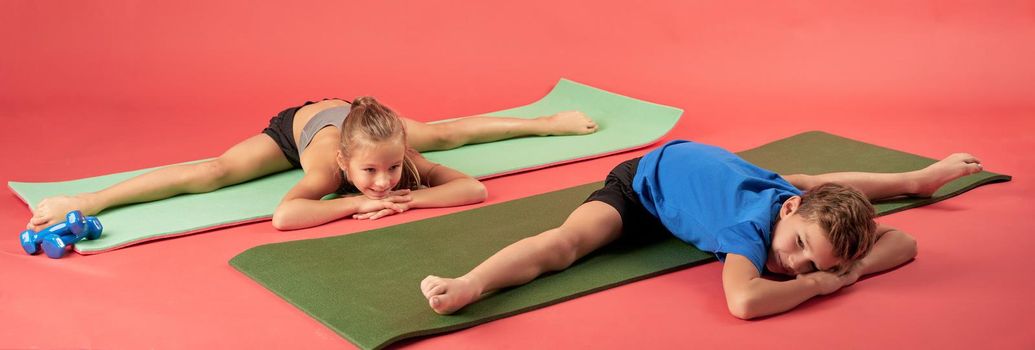 Cute kids in sportswear looking away and smiling while doing stretching exercise on yoga mats