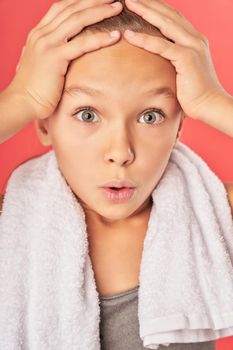 Close up of adorable girl with towel around her neck looking at camera with astonished expression