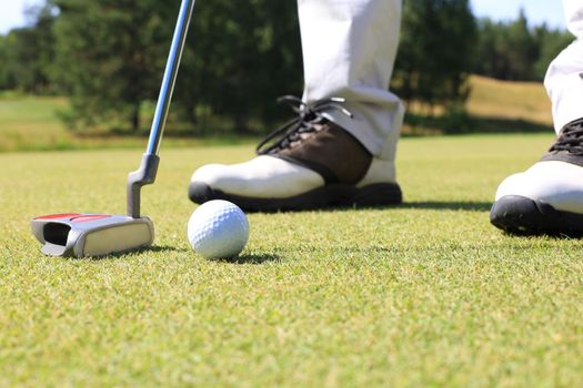 Golf player at the putting green hitting ball into a hole