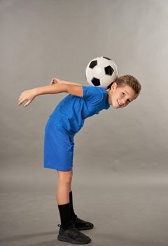 Adorable male child football player looking at camera and smiling while doing soccer trick