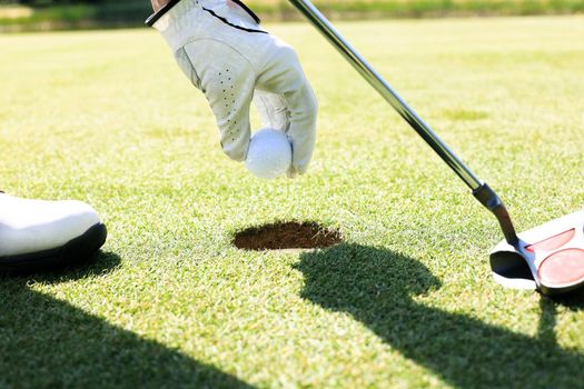 Golf player takes the ball out of the hole