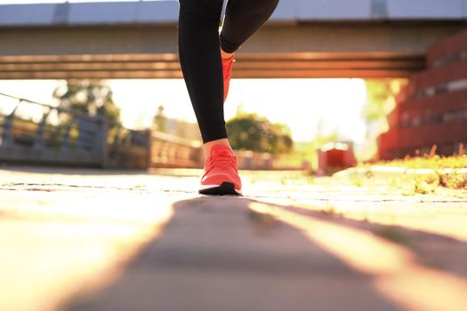 Close up of young woman in sports shoes jogging while exercising outdoors