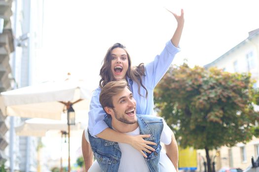 Handsome young man carrying young attractive woman on shoulders while spending time together outdoors