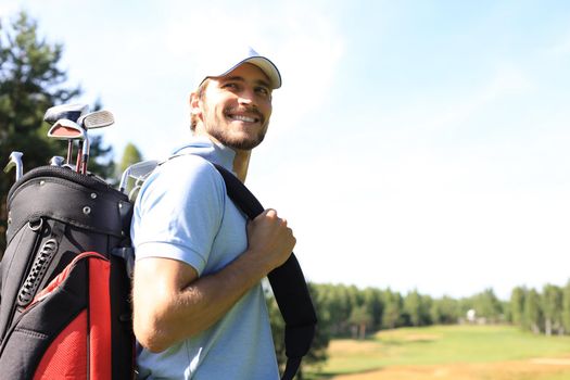 Golf player walking and carrying bag on course during summer game golfing