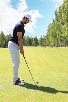 Full length of golf player playing golf on sunny day. Professional male golfer taking shot on golf course