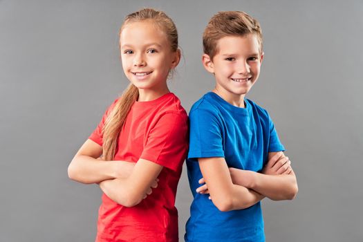 Adorable siblings looking at camera and smiling while standing back to back and crossing arms