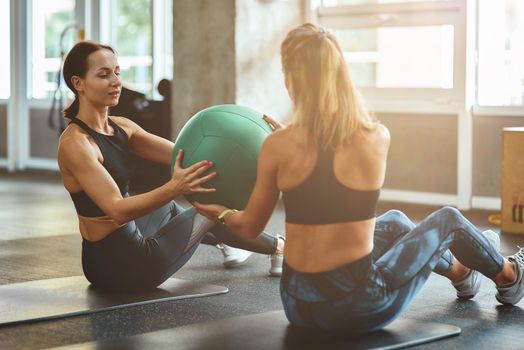 Working out together. Two young athletic women in sportswear exercising with ball at gym. Sport, training, wellness and healthy lifestyle