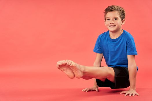 Adorable male child in sportswear looking at camera and smiling while lifting himself up and balancing on two hands