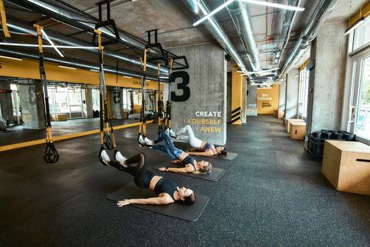 Strength training. Three young caucasian athletic women in sportswear exercising with fitness trx straps at industrial or crossfit gym. Sport, people working out, wellness and healthy lifestyle