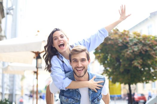 Handsome young man carrying young attractive woman on shoulders while spending time together outdoors