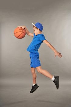 Cute male child in sportswear jumping in the air and holding basketball ball