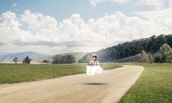 Young little boy keeping eyes closed and looking concentrated while meditating on cloud above the road with beautiful and breathtaking landscape on background.