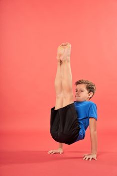 Cute male child on sportswear balancing on two hands and lifting legs up while practicing yoga