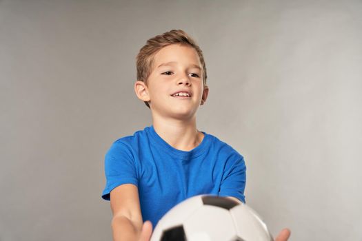 Cheerful male child in blue shirt looking away and smiling while playing with football ball