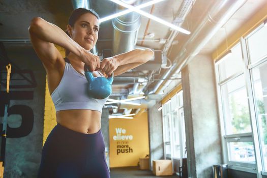 Working hard. Young strong athletic woman in sportswear exercising with dumbbell at industrial gym, training arms. Sport, workout and healthy lifestyle