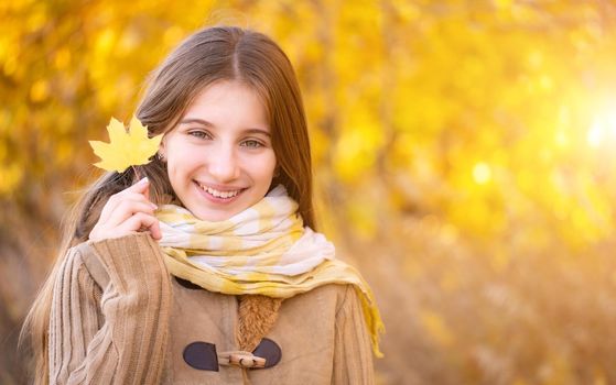 Portrait of happy girl with yellow leaf on autumn background