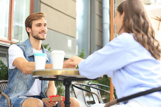 Smiling young girl having a date with her boyfriend at the coffee shop, man holding present box