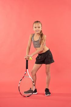 Adorable female child wearing crop top and shorts while holding tennis racket and smiling