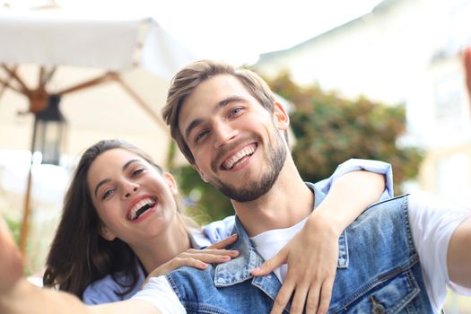 Beautiful lovely young couple walking at the city streets, hugging while taking a selfie