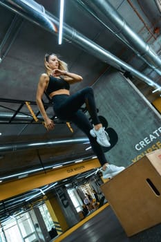 Fitness workout. Full length young athletic woman in sportswear jumping on wooden crossfit box at gym. Sportive people, healthy lifestyle and workout concept