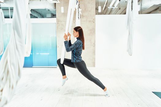 Harmony and balance. Young caucasian fitness woman in sportswear practicing fly yoga in beautiful bright studio. Sport, wellness and healthy lifestyle, aerial yoga concept