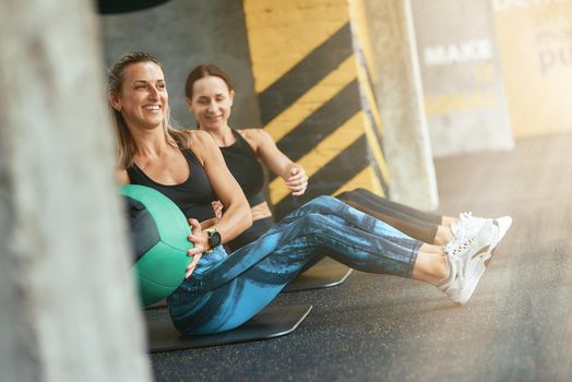 Two young happy athletic women in sportswear exercising with fitness ball at gym, working out together. Sport, training, wellness and healthy lifestyle