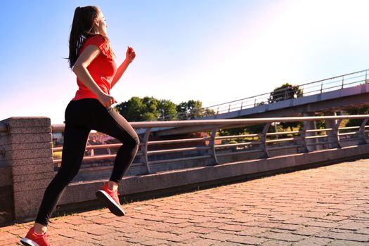 Photo of modern young woman in sports clothing jumping while exercising outdoors