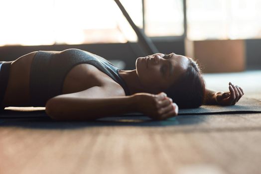 Exhausted fitness woman in sportswear lying on the floor at gym, keeping eyes closed and resting after workout, taking a break during training. Sport, wellness and healthy lifestyle