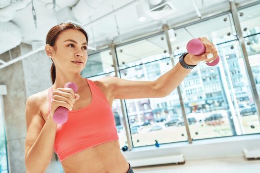 Healthy lifestyle. Young beautiful fit woman in sportswear exercising with dumbbells in fitness studio or gym. Sport, training and workout concept