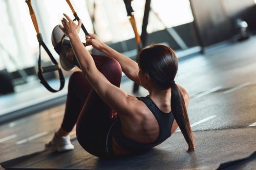 Young athletic woman in sportswear exercising with fitness trx straps at industrial gym, suspension training. Sport, workout, wellness and healthy lifestyle