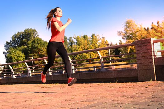 Young attractive sporty fitness woman running while exercising outdoors at sunset or sunrise