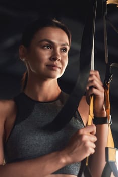 Workout. Vertical shot of a young attractive woman holding trx fitness straps while exercising at industrial gym. Sport, wellness and healthy lifestyle