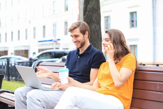 Attrative young couple using laptop computer while sitting on a bench outdoors