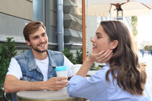 Attractive young couple in love drinking coffee while sitting at the cafe table outdoors